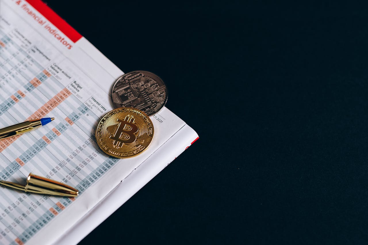 A close-up of Bitcoin with financial indicators and a pen on a black surface.